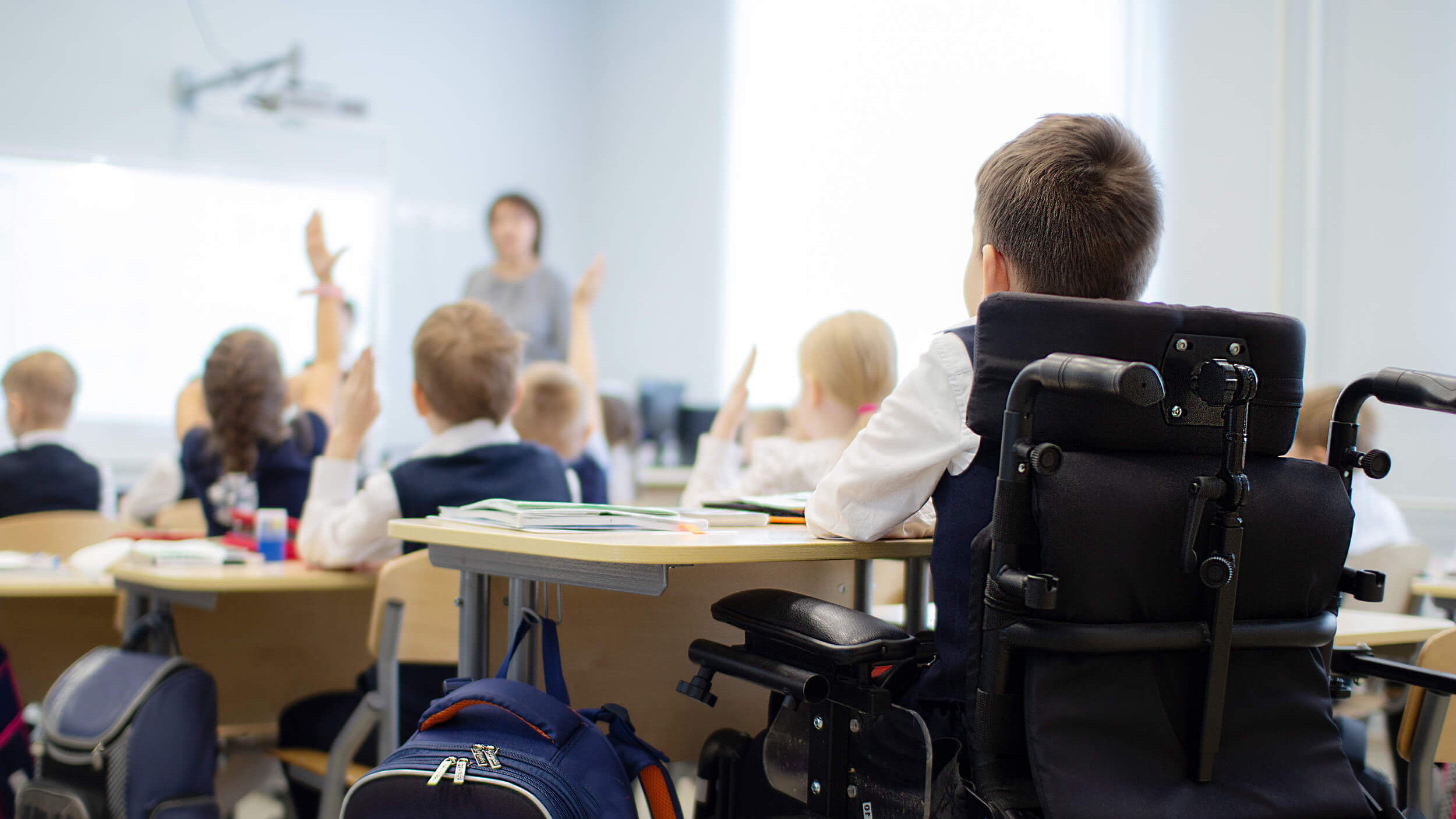 Ein Bub in einem Rollstuhl sitzt gemeinsam mit anderen Kindern in einer Schulklasse.